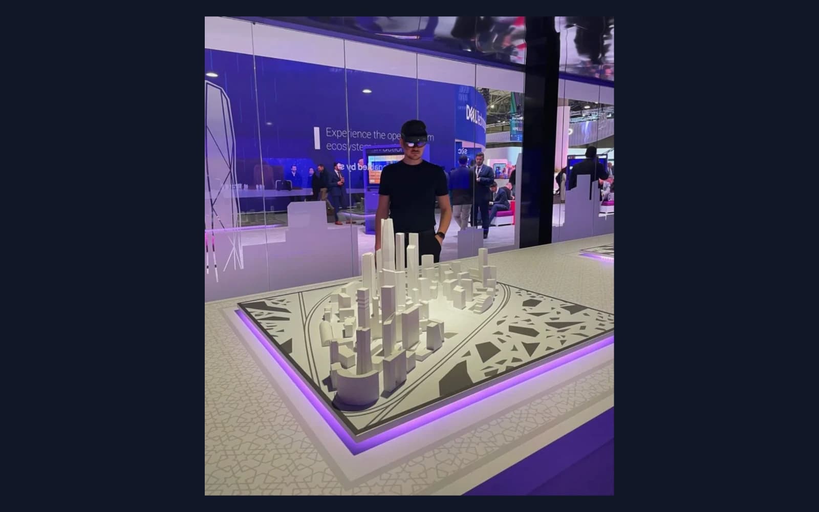 A visitor wearing a Microsoft HoloLens stands over the physical model city at stc's Mobile World Congress stand, with the exhibition hall behind him.